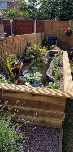 an outdoor pond in the middle of a garden with plants and flowers around it, next to a wooden fence