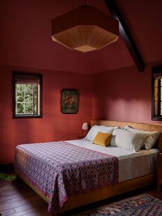 a bed in a room with red walls and wooden flooring next to two windows