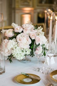 the table is set with white and pink flowers in vases, silverware, and candles