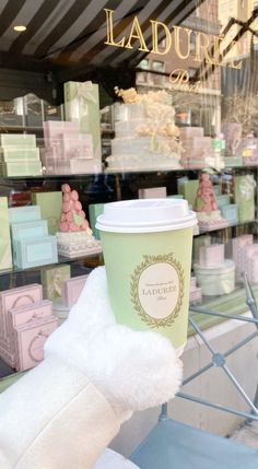 a teddy bear holding up a cup of coffee in front of a storefront window