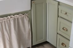 a white sink sitting under a window next to a counter top with a curtain on it