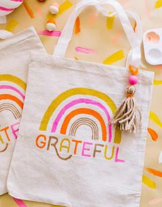 two white bags with the words grateful and a rainbow painted on them next to confetti