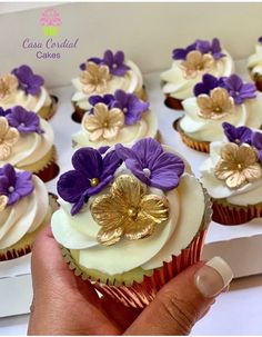 cupcakes with white frosting and purple flowers are being held by a hand