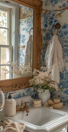 a bathroom sink sitting under a large mirror next to a white vase filled with flowers