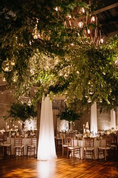 an indoor wedding venue with tall trees and white linens on the tables, surrounded by greenery