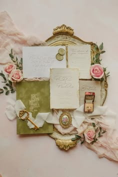 wedding stationery with pink roses and gold accents on a vintage mirror, surrounded by flowers