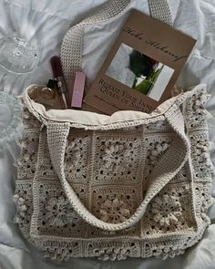 a crocheted bag with a book and some lipstick on it sitting on a bed