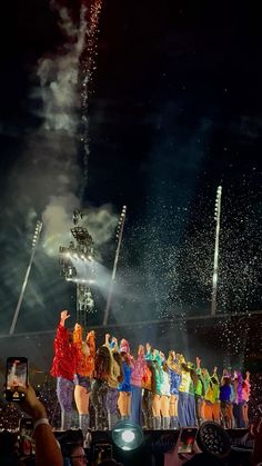 a group of people standing on top of a stage under a sky filled with fireworks