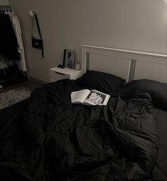 an open book sitting on top of a black comforter covered bed in a bedroom