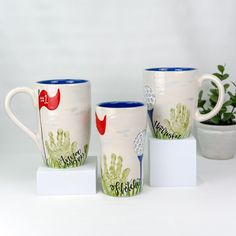 three coffee mugs sitting next to each other in front of a potted plant