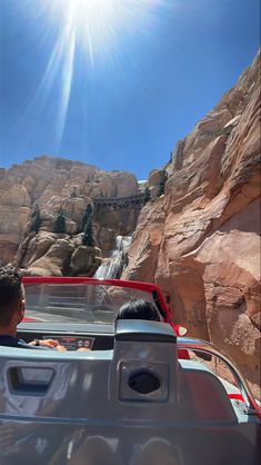 two people are driving in the back of a pick - up truck near a waterfall