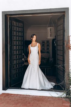 a woman in a white wedding dress standing at the entrance to a room with open doors