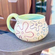 a ceramic mug sitting on top of a wooden table next to a door with flowers painted on it