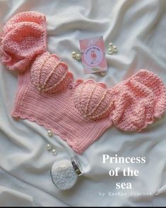 a pink knitted hat and diaper on top of a white sheet with pearls