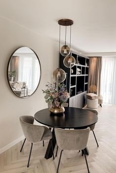 a dining room table with four chairs and a round mirror on the wall above it