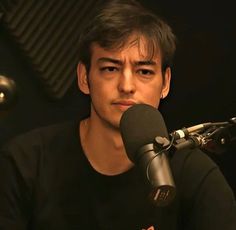 a young man is sitting in front of a microphone and looking at the camera with an intense look on his face