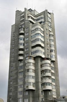 a tall building with multiple balconies on the top and bottom floors, in front of a cloudy sky