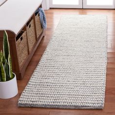 a white rug on the floor in front of a door with baskets and a plant next to it