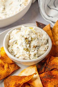 a white plate topped with chips and dip next to a bowl filled with cream cheese