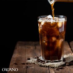 iced coffee being poured into a glass on top of a wooden table next to beans