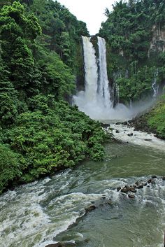 a large waterfall in the middle of a forest filled with trees and water flowing down it's sides