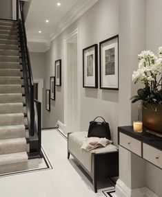 a white and black hallway with flowers on the table next to the stairs leading up to the second floor