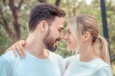 a man and woman standing close to each other in front of trees with their arms around one another