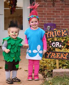 two children dressed in costumes standing next to a trick or treat sign