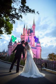 a bride and groom standing in front of a castle at night with balloons flying around them