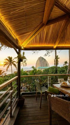 an outdoor dining area with tables and chairs overlooking the ocean at sunset in front of a mountain