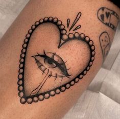 a heart shaped tattoo with an eye and beads on the side of its leg,