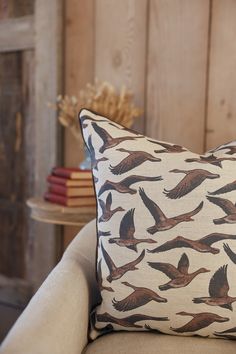 a pillow with birds on it sitting on a chair in front of a wooden wall