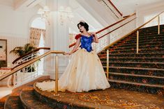 a woman in a blue and white dress is standing on some stairs with her hand on the railing