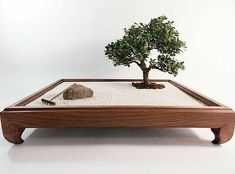 a bonsai tree in a wooden tray with white sand and rocks on the bottom