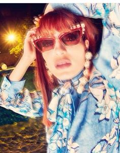 a woman with red hair wearing sunglasses and a blue floral shirt is posing for the camera