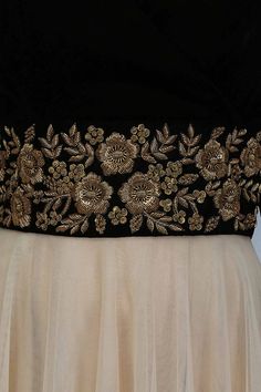 a woman wearing a black and gold dress with floral appliques on the waist