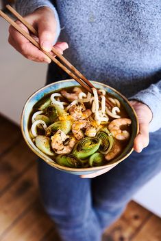 a person holding a bowl of food with chopsticks