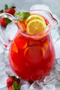 a pitcher filled with red liquid and sliced lemons on top of ice next to strawberries