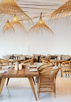 a dining room with wicker chairs and tables in the center is decorated with hanging lights