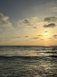 the sun is setting over the ocean with some clouds in the sky and water around it