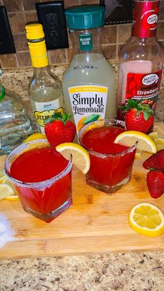 two glasses filled with liquid and strawberries on top of a cutting board next to lemons