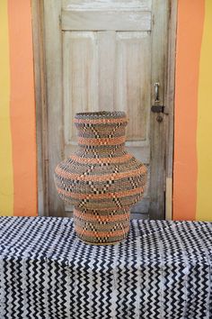 a vase sitting on top of a table next to a wooden door with an orange and black checkered cover