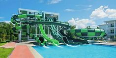 a large green water slide in the middle of a swimming pool next to a building