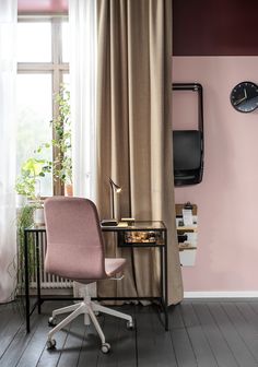 a pink chair sitting in front of a window next to a desk with a clock on it