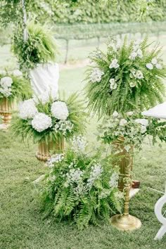 an outdoor ceremony setup with white flowers and greenery in gold vases on the grass