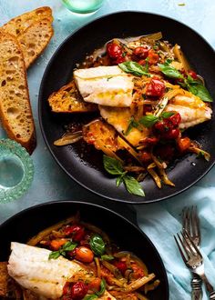 two black plates filled with fish and vegetables on top of a blue table cloth next to slices of bread