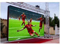 a large television screen showing a soccer game on it's display wall in front of a stadium