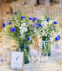 blue and white flowers are in vases on a table with wine glasses, place cards and silverware