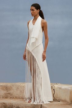 A halter neck dress with draped fabric over the shoulders and a semi-fitted bodice. Cut from 100% cotton jersey, it features an asymmetrical hemline detailed with handwoven macrame and a fringe skirt that falls down around the ankles. Style the Bebe Bikini Bottom underneath and add a simple leather sandal for a unique approach to occasionwear. Asymmetrical Maxi Dress, Maxi Dress White, Macrame Dress, Halter Neck Dress, Maxi Dress Sale, Simple Leather, Fringe Skirt, Fringe Dress, Halterneck Dress