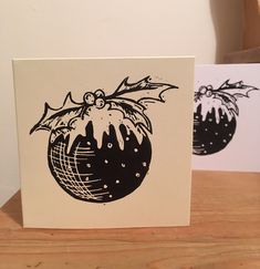 two christmas cards with black and white designs on them sitting on a wooden table next to each other